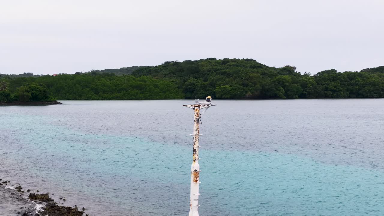 Una lenta panoramica rivela un segnalatore di navigazione deteriorato vicino a una costa lussureggiante di un'isola tropicale