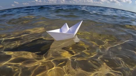 delicate white origami boat gently rocking on pristine water surface, navigating calm waves beneath expansive blue sky with soft white clouds, symbolizing journey and peaceful exploration