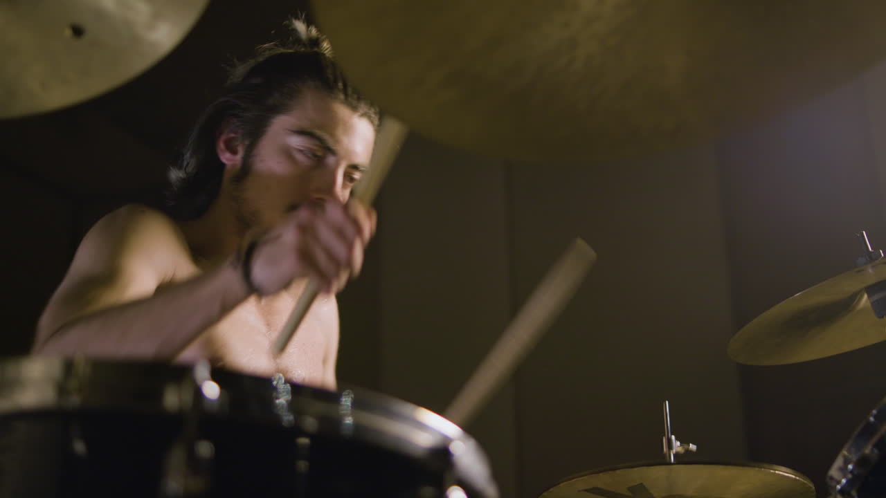 baterista masculino sin camisa enérgico con barba tocando la batería