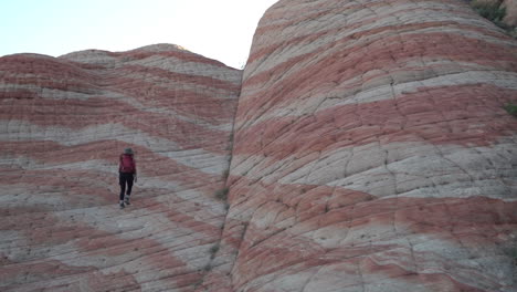 female hiker walking uphill on strange swirled layered sandstone patterns, slow motion