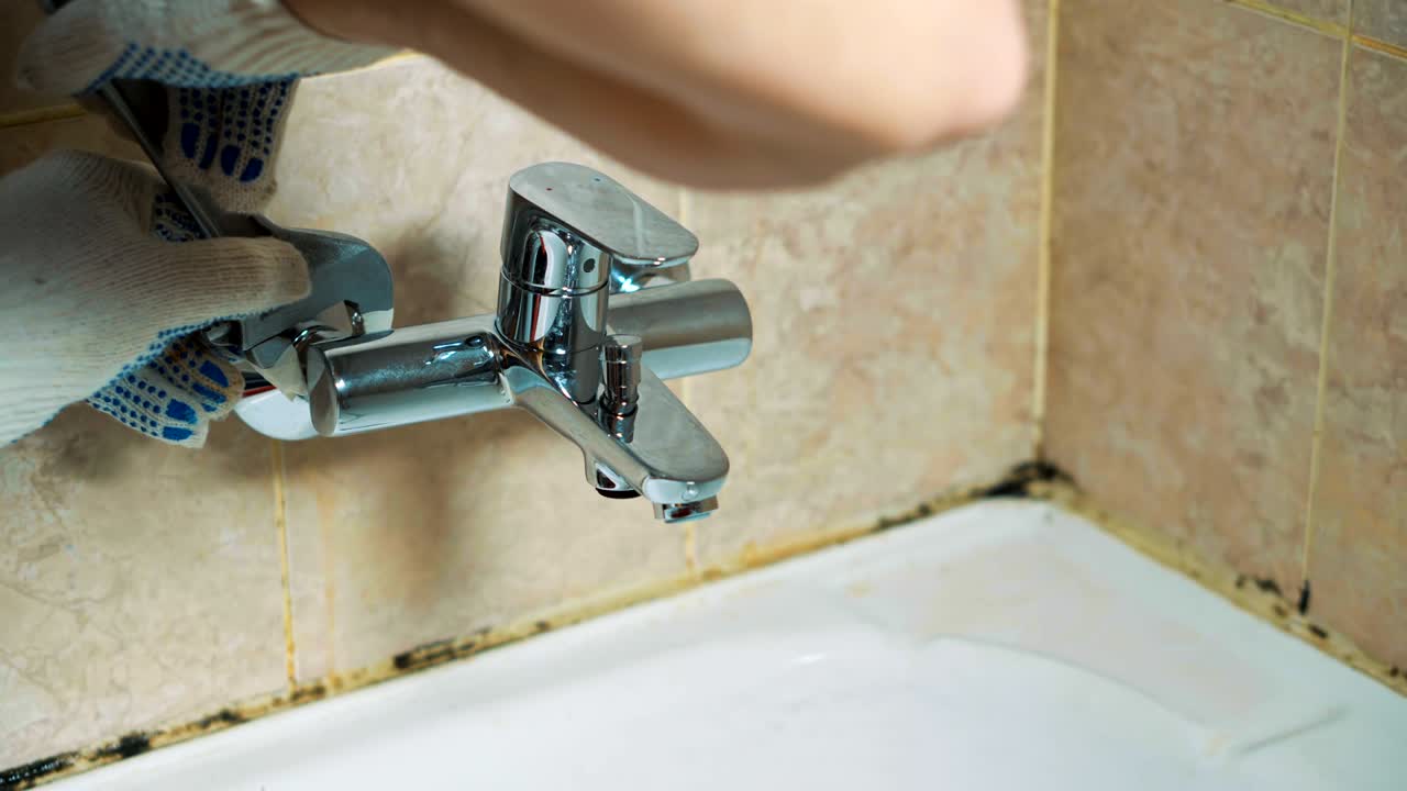 las manos con guantes del fontanero instalan el grifo en el baño.