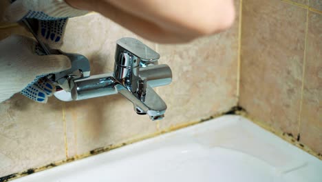 close-up gloved hands of the plumber installs the faucet in the bathroom.