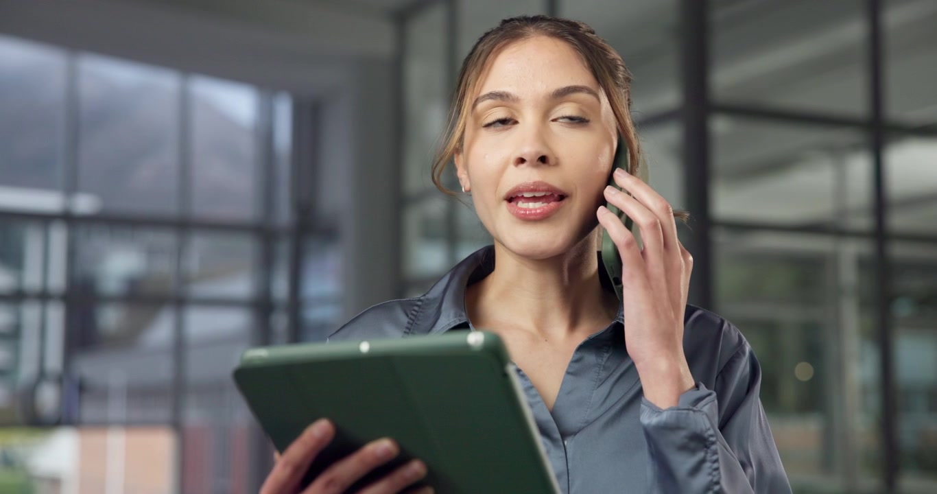 Profesjonell kvinne som snakker i smarttelefon mens hun bruker et nettbrett på kontoret