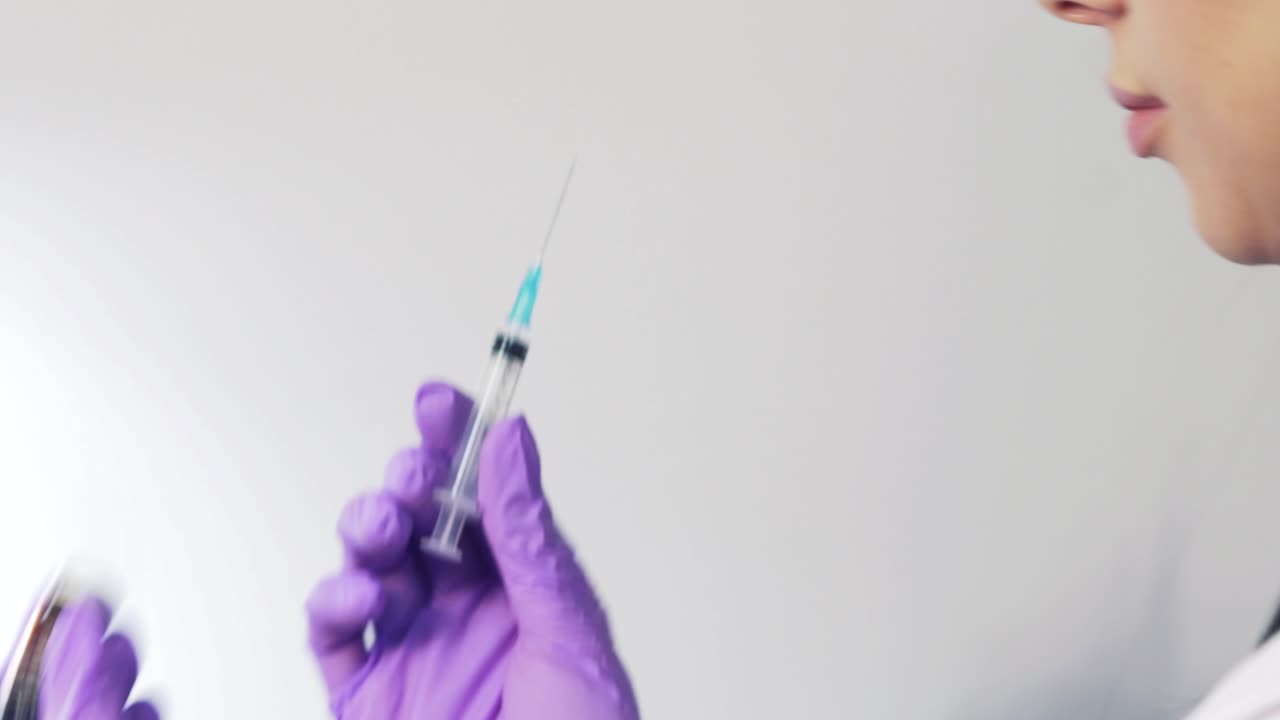Female doctor in purple gloves drawing up solution from vaccine bottle and filling syringe injection