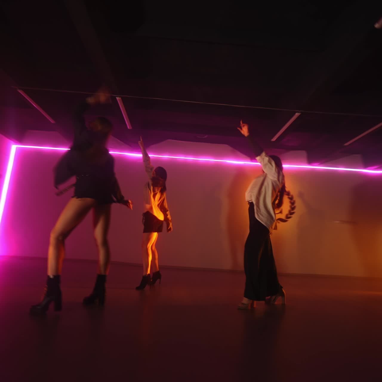 Dancing trio performing in the studio with pink light. Girls dance actively on high hills. Low angle view