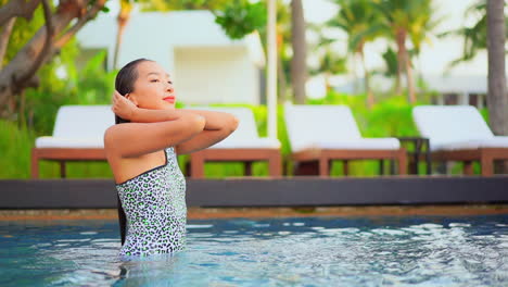 Emergiendo-Del-Agua-Tibia-De-La-Piscina-En-Un-Lujoso-Resort,-Una-Mujer-Joven-Se-Aparta-El-Cabello-Mojado-De-La-Cara