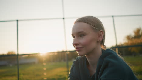 young lady in green hoodie engaged in outdoor sport activity, sunlight creating a golden glow around her shoulders with open field and fence in the background during golden hour