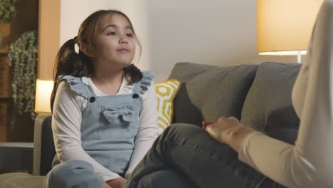 teacher or parent teaching young girl sign language sitting on sofa at home