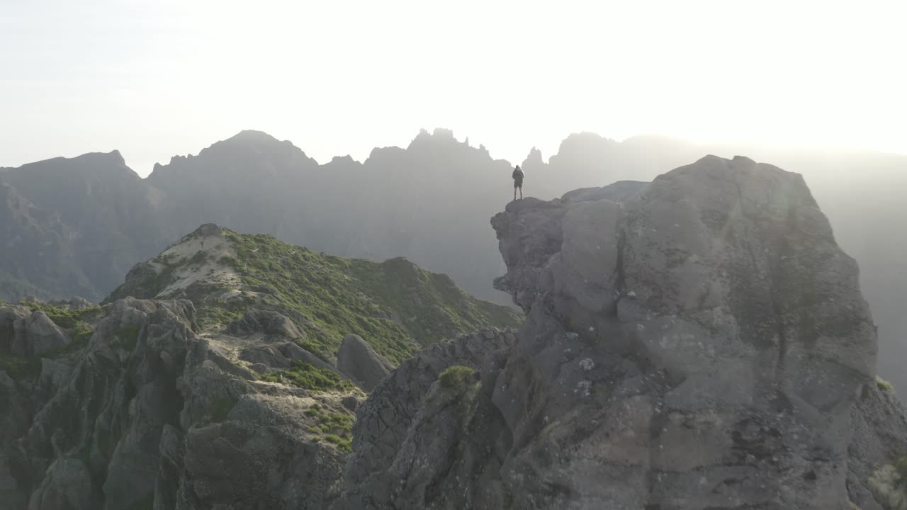 un hombre está parado solo en el borde de la montaña pico grande en madeira durante un amanecer sobre el hermoso paisaje