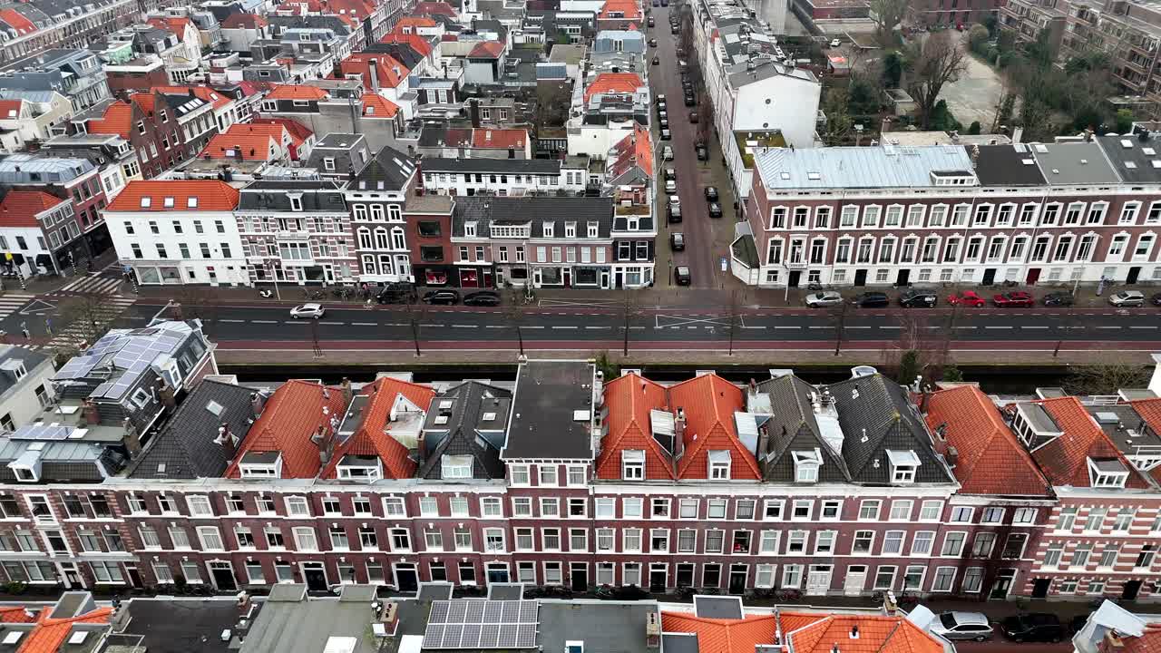 Row of charming historic townhouses and apartments in Dutch neighborhood. Aerial lateral wide shot. Driving car on road in The Hague city, Netherlands.