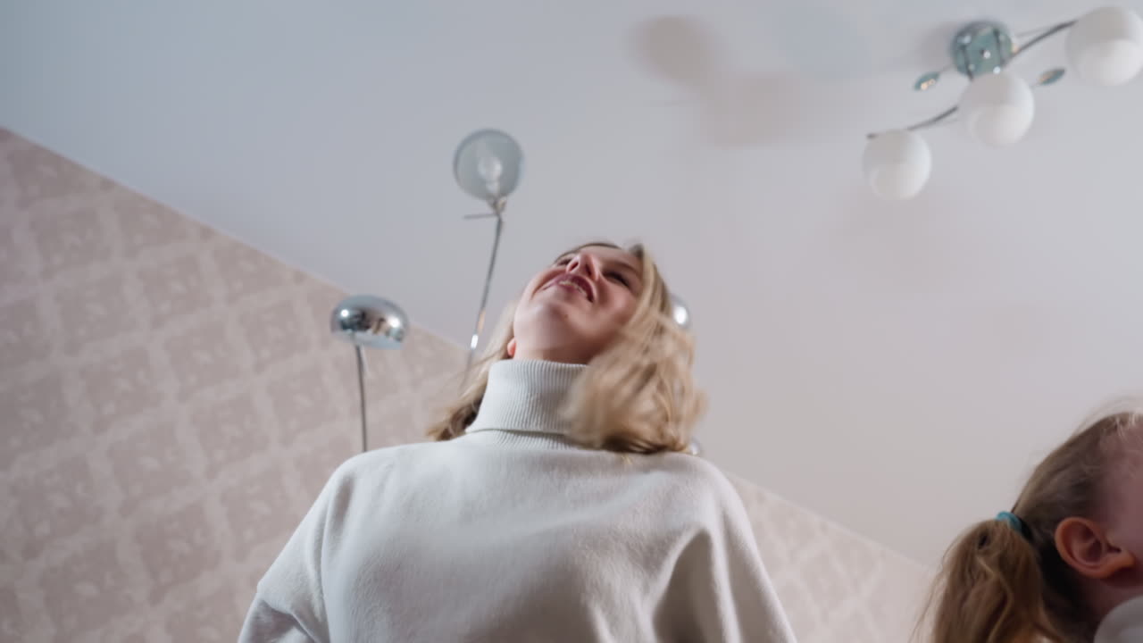 Young woman in white sweater raising arm upward with energetic motion, expressive body language viewed from low angle, symbolizing empowerment, freedom, lifestyle energy, indoor moment
