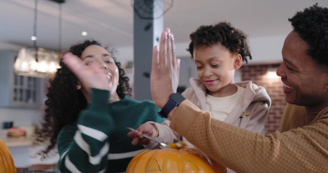Famiglia afroamericana che prepara una zucca a casa, con un viso disegnato, mentre esorta il bambino a raccogliere i semi in una pentola