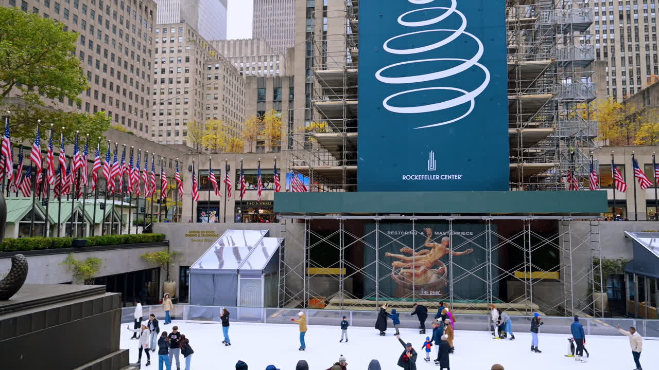 New York, USA, 8 novembre 2025: pista e bandiere del Rockefeller Center. Una statua in bronzo si affaccia sulla pista di pattinaggio su ghiaccio e sulla piazza con le bandiere del Rockefeller Center a Midtown, Manhattan