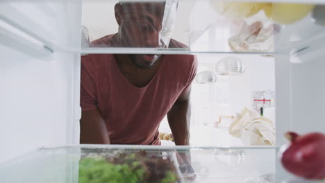 vista mirando desde el interior del refrigerador mientras el hombre abre la puerta y desembala la bolsa de compras de alimentos