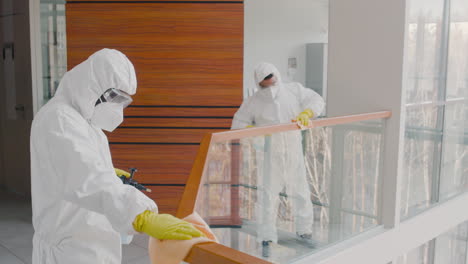 two cleaning men wearing personal protective equipment cleaning stair railings inside an office building