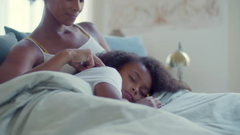 close up of little black girl lying on her mum's knees in bed, then opening her eyes and smiling