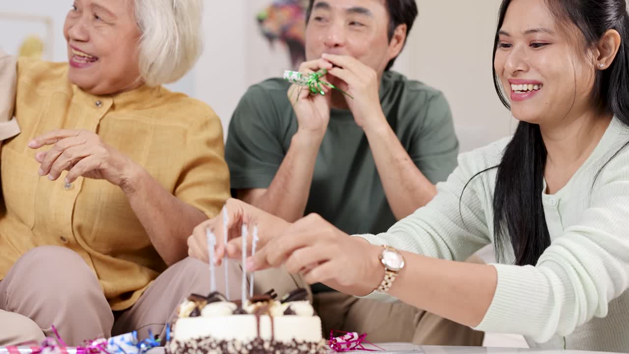 Elderly woman celebrates birthday with family, cake, candles, and laughter in a cozy home