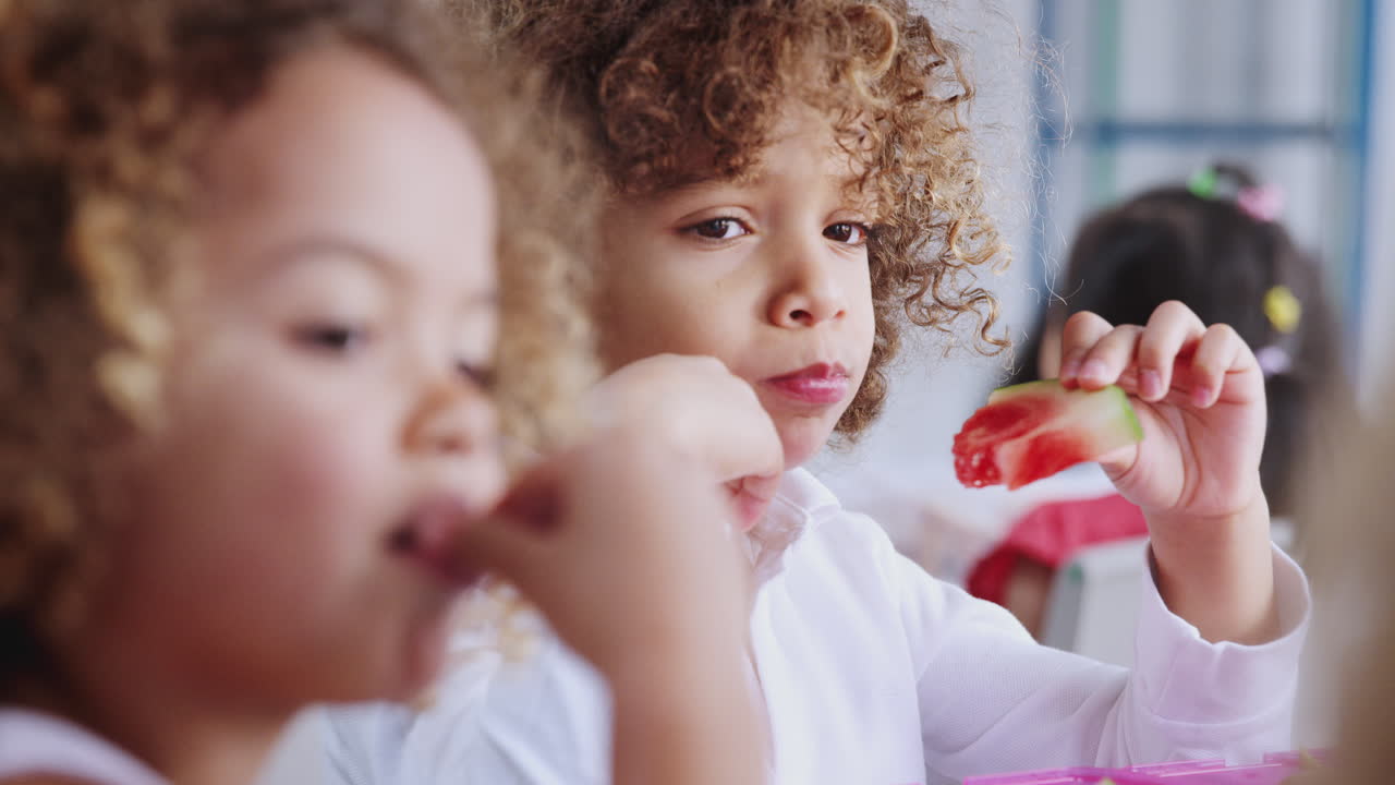 Primo piano di bambini che mangiano insieme i loro pranzi al sacco alla scuola dell'infanzia, con cambio di messa a fuoco
