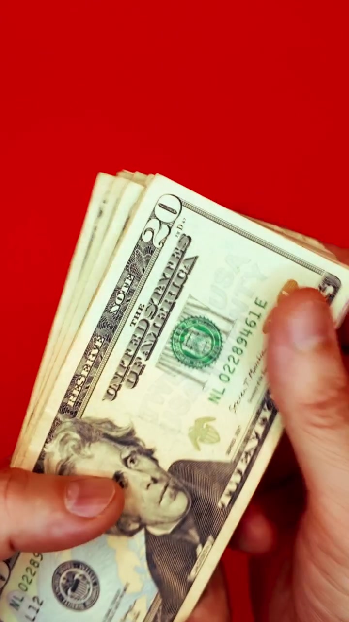 B-roll verticale 9:16: mani che sventolano banconote da 20 dollari su sfondo rosso. Concetto per denaro veloce, motivazione alla ricchezza, transazione illegale, pagamento dello stipendio, affari del dark web e successo finanziario.