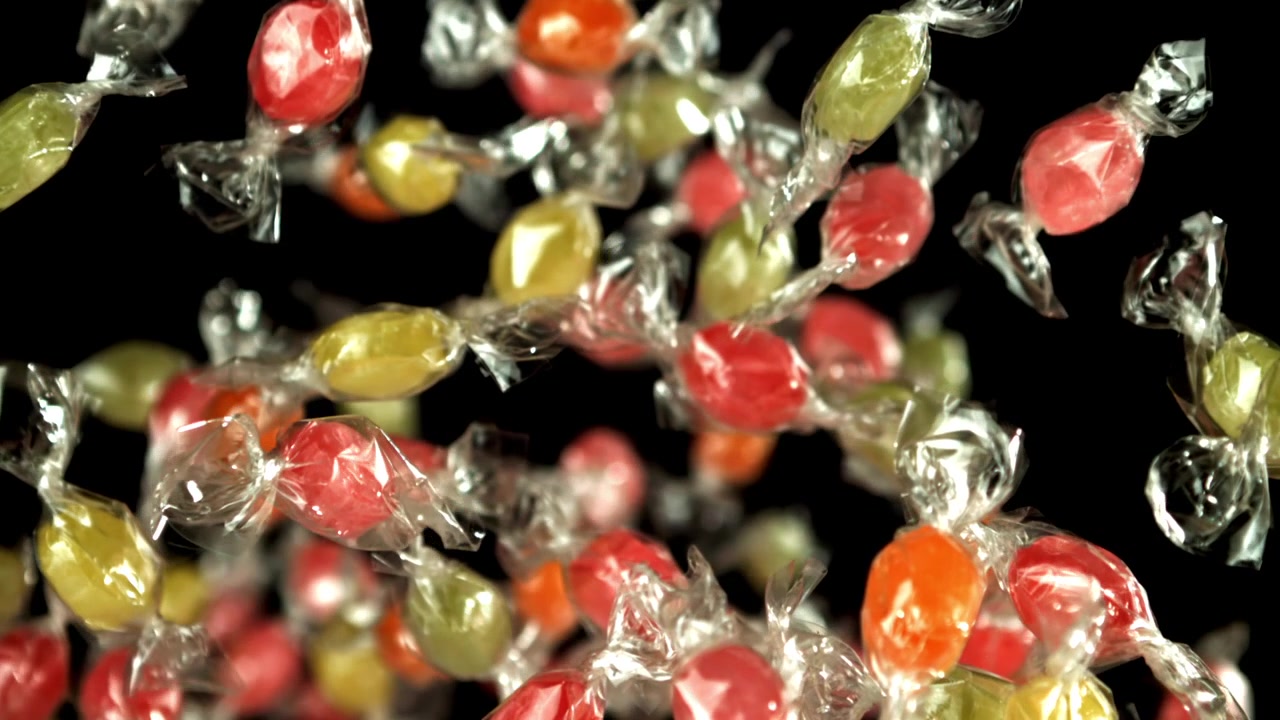 Doces coloridos embalados caindo em câmera lenta sobre fundo preto.
