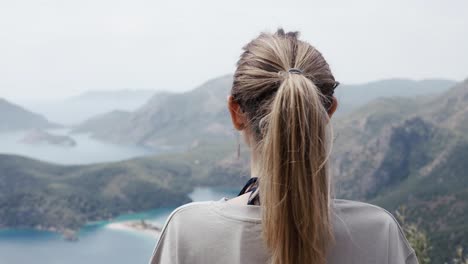 back iew of calm woman on top of a beautiful mountain valley enjoying the outdoor scenery