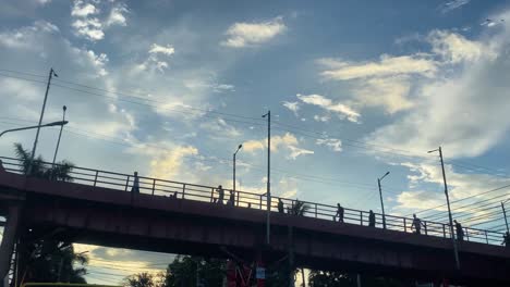 Mirando-Hacia-La-Silueta-De-La-Gente-Caminando-Por-El-Puente-En-Sylhet-Con-El-Cielo-Azul-Y-Las-Nubes-En-El-Fondo