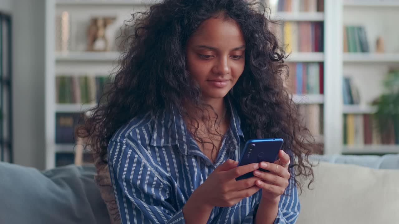 Close up of young happy smiling indian woman chatting on mobile phone on sofa