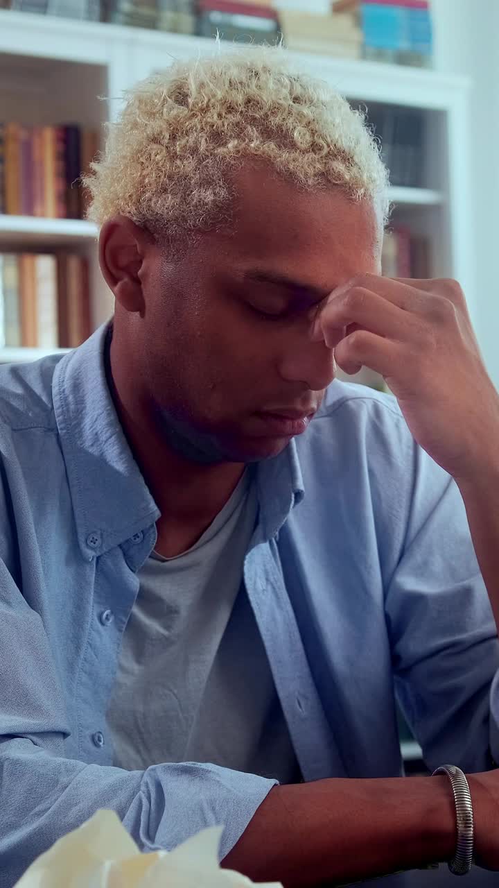 Stressed young african man rubbing his forehead at a home office desk