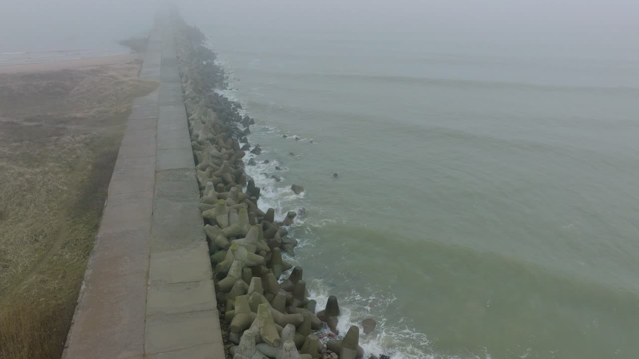 воздушное наблюдение за портом лиепая, бетонная пристань, побережье балтийского моря, туманный день с густым туманом, настроение, большие штормовые волны, брызги, широкий снимок с дрона с высоты птичьего полета, движущийся вперед