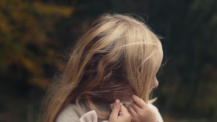 Graziosa bambina che si districa i lunghi capelli biondi, ritratto, al rallentatore