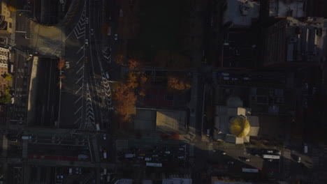 Aerial-birds-eye-overhead-top-down-panning-view-of-vehicles-driving-in-streets-of-city.-Autumn-colour-trees-along-multilevel-road-intersection.-Manhattan,-New-York-City,-USA