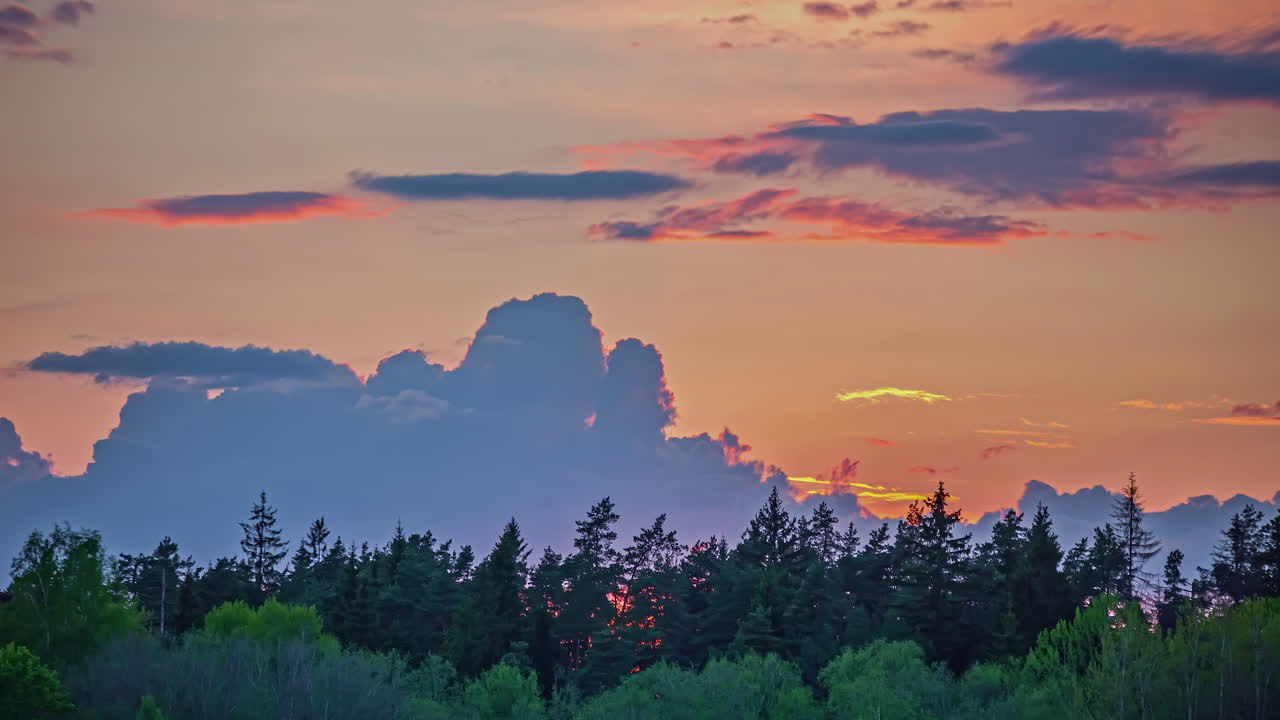 Static shot of sunset in the background over Yellow Sky behind lush green forest in timelapse