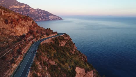 a car is driving on the amalfi coast road during sunset followed by a drone