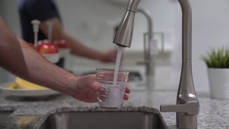 Filling-up-glass-with-fresh-tap-water-at-sink-in-clean-kitchen-for-sustainable-environment