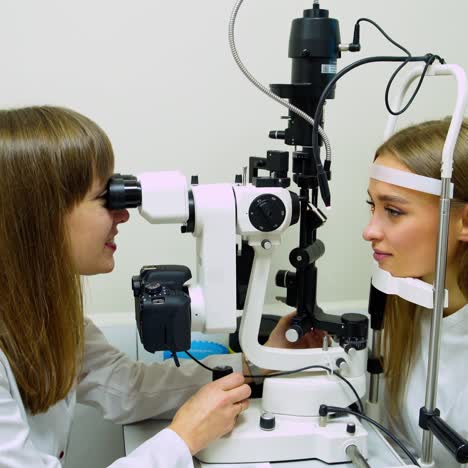 woman checks her eyesight with optical equipment. professional optometrist looking into patient's eye through the the special device in clinic.