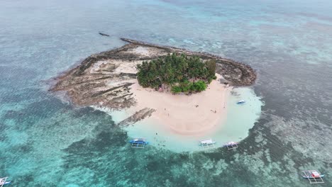 aerial drone orbit over guyam island, siargao islands, philippines, reveals a lush palm-covered islet encircled by turquoise shallows and coral reefs in the pacific ocean, near general luna town