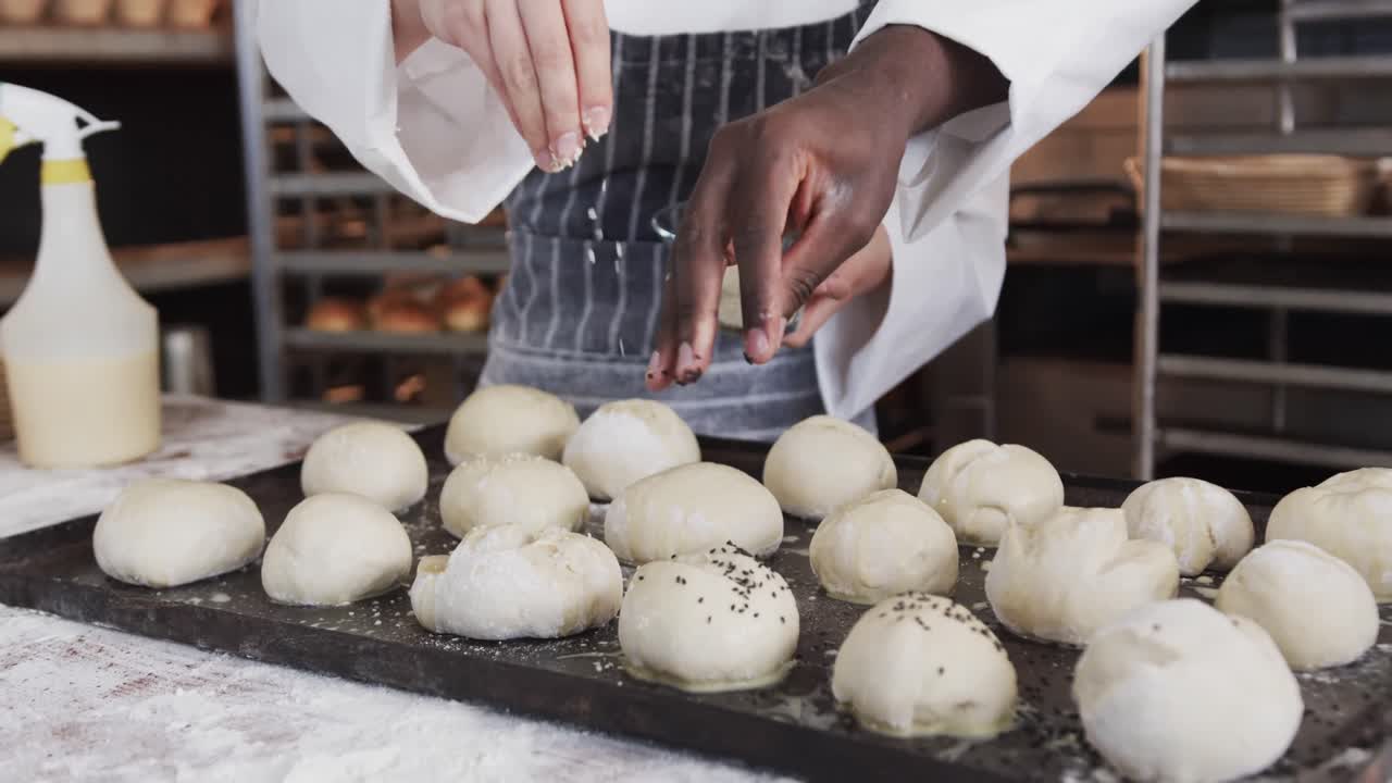Diverse bakers working in bakery kitchen, sprinkling poppy seeds on rolls in slow motion