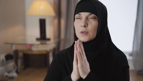 camera moving around young beautiful muslim woman praying at home. lady in hijab sitting holding hands together and talking. lifestyle, religion. camera moving around from left to right.