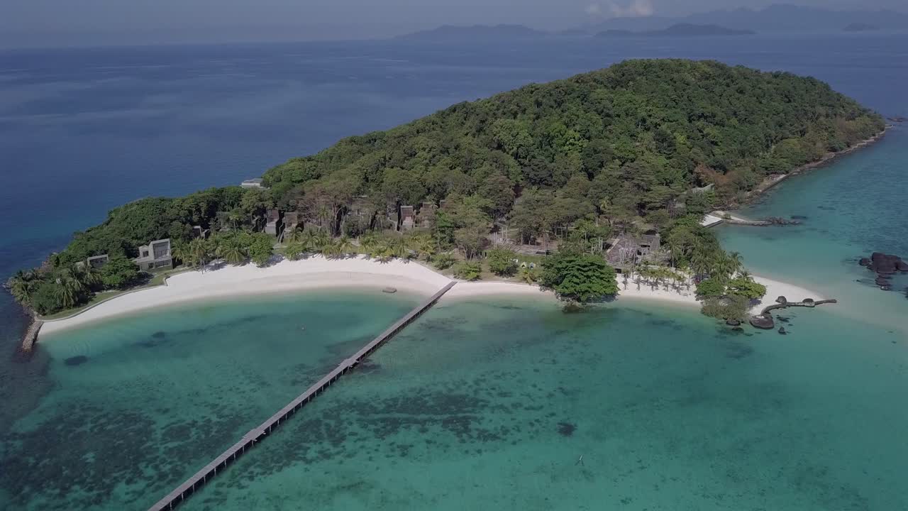 Birdseye Aerial view forward towards pier and over tropical white sand beach and greenery of paradise island Koh Kham,Thailand. Full view of the island.