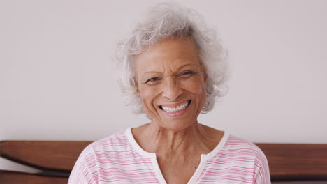 Porträt-Einer-Lächelnden-älteren-Frau,-Die-Zu-Hause-Auf-Der-Seite-Des-Bettes-Sitzt-Und-Positiv-Aussieht