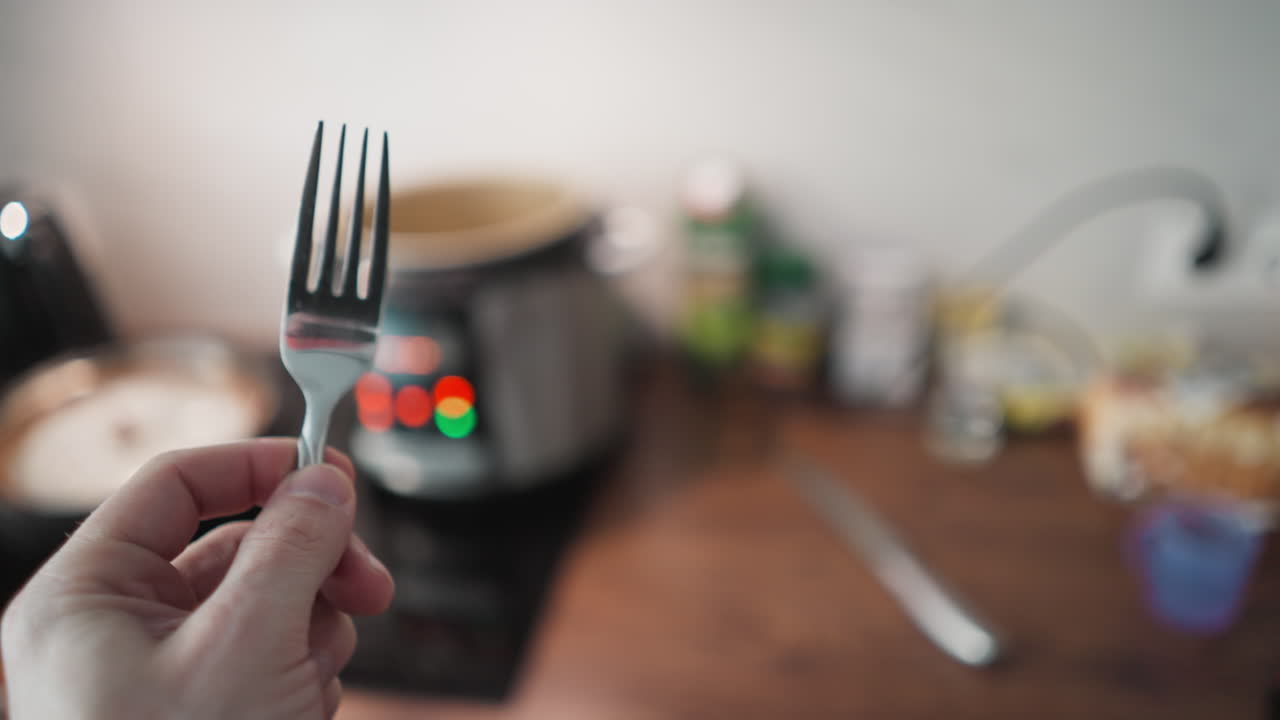 pov de una persona con un tenedor acercándose a una mesa de cocina con una cocina múltiple parpadeando luces en el fondo, filmado con una cámara de mano