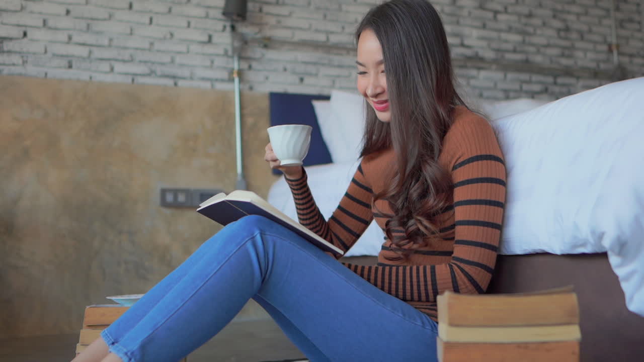 침실 바닥에서 책을 읽는 동안 젊은 여성이 차를 마신다