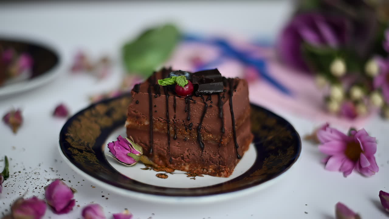 This delightful chocolate cake is beautifully presented with fresh mint and berries on a decorative plate. Surrounded by colorful flowers, it showcases a tempting dessert perfect for any occasion