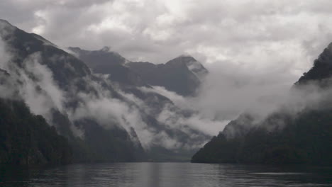 Slow-motion-pan-across-misty-and-cloudy-mountains-in-Doubtful-Sound-with-water-in-foreground---Patea,-New-Zealand