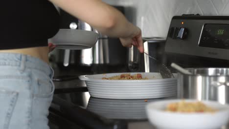 A-caucasian-woman-grabs-a-white-bowl-and-serves-up-pasta-into-the-bowl