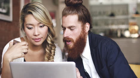 Young-couple-shopping-online-using-digital-tablet-computer-in-cafe