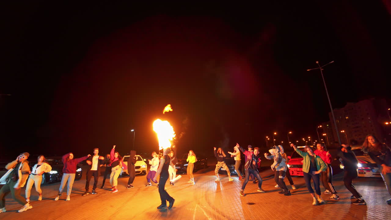 Fire show in the circle of dancing people. Man with a torch in the middle, teenagers around perform hip hop. Low angle view.