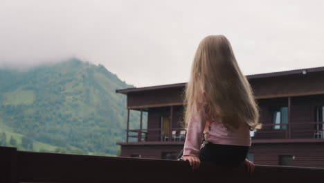 cute little girl sits on railing against distant mountains