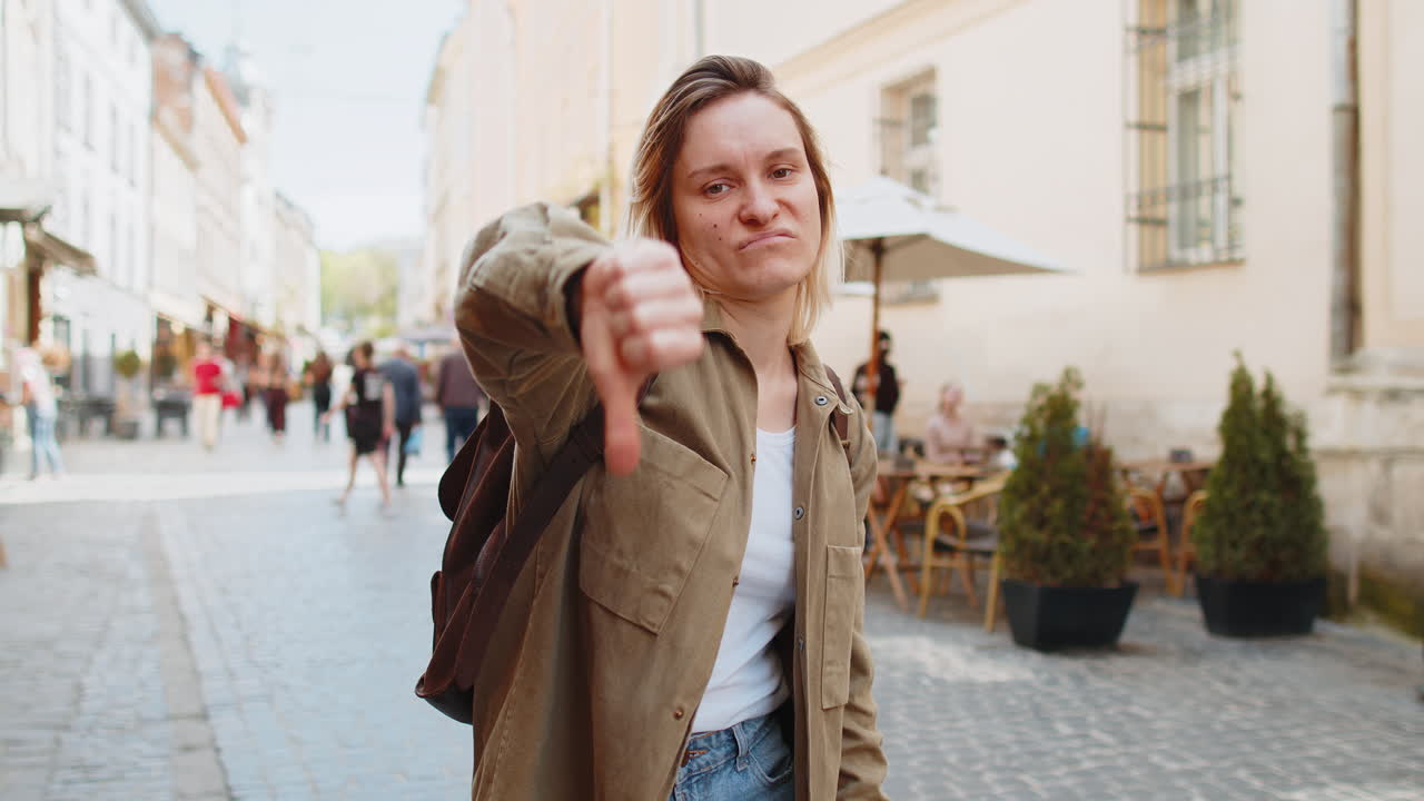 Giovane donna sconvolta che mostra il pollice in giù segno di disapprovazione insoddisfatta cattivo feedback sulla strada della città