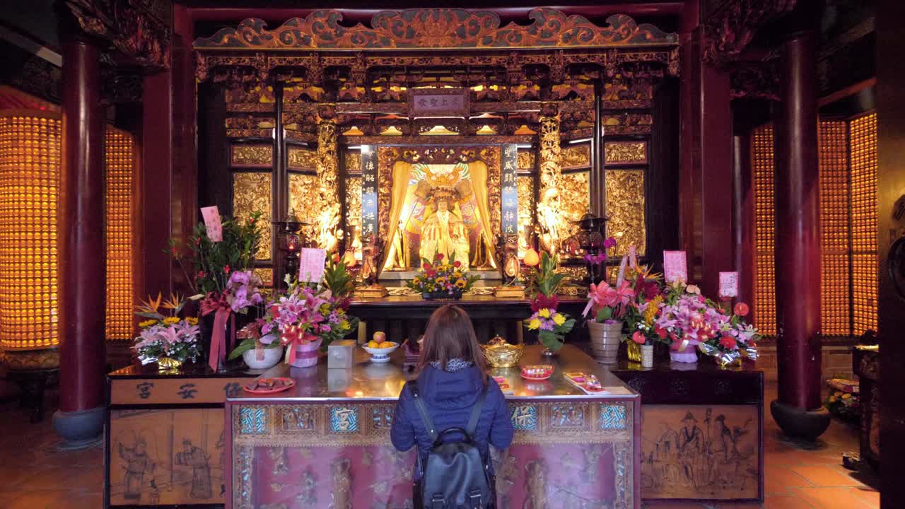 Slow motion shot of woman praying at Dalongdong Baoan Temple in Taipei, Taiwan - camera tracking backwards